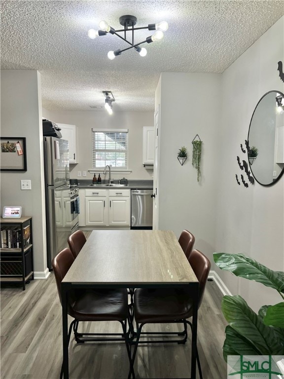 dining room featuring an inviting chandelier, a textured ceiling, light wood-type flooring, and sink