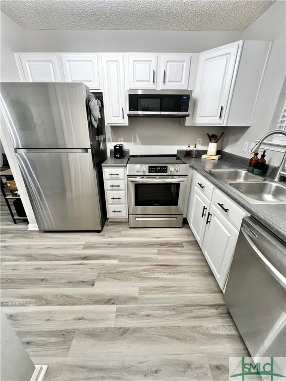 kitchen featuring sink, a textured ceiling, white cabinetry, stainless steel appliances, and light wood-type flooring