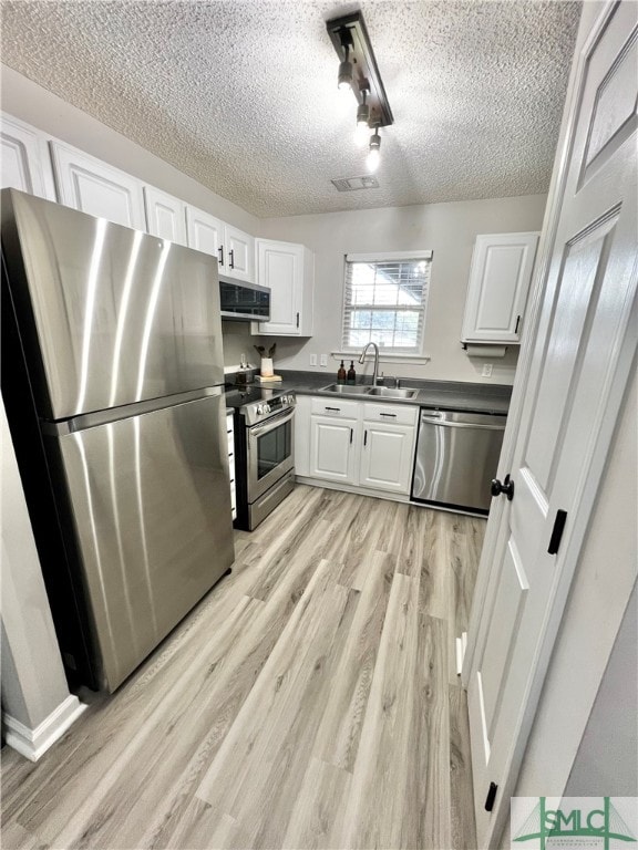 kitchen with a textured ceiling, light hardwood / wood-style floors, sink, white cabinetry, and appliances with stainless steel finishes