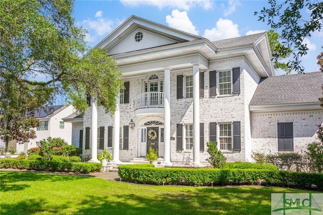 greek revival inspired property with a balcony and a front yard