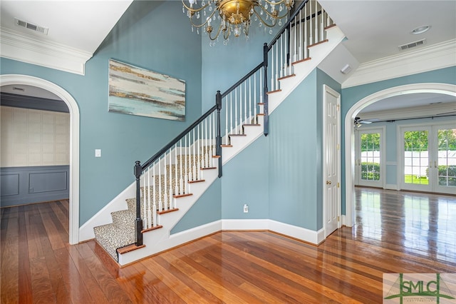 stairway with french doors, hardwood / wood-style flooring, a notable chandelier, and ornamental molding