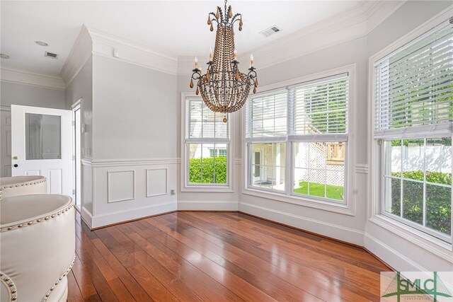 unfurnished dining area featuring crown molding, a wealth of natural light, wood-type flooring, and a notable chandelier