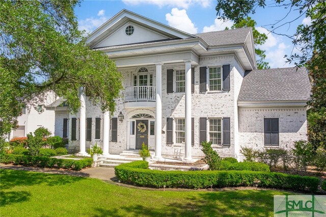 neoclassical home featuring a front lawn and a balcony