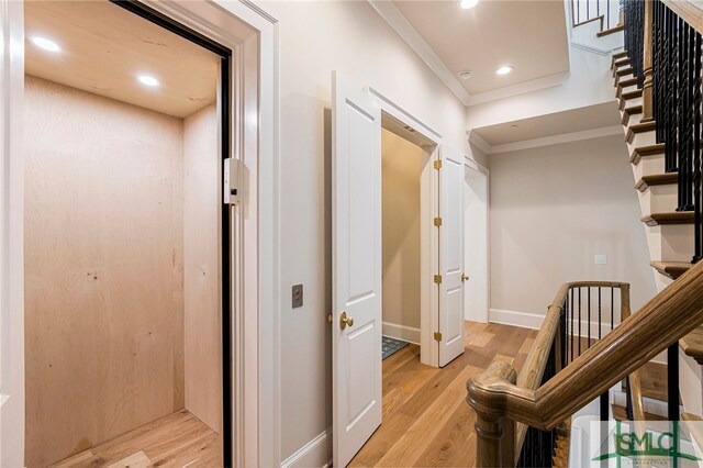 hallway featuring light wood-type flooring, ornamental molding, and elevator