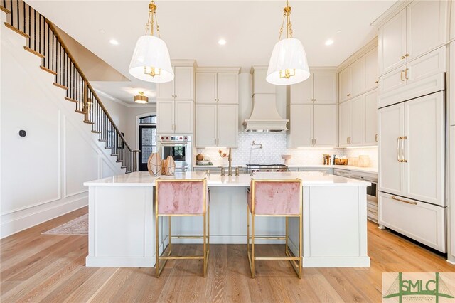 kitchen featuring hanging light fixtures, stainless steel appliances, an island with sink, and light hardwood / wood-style flooring