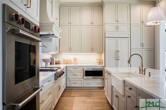 kitchen featuring custom range hood, light hardwood / wood-style flooring, appliances with stainless steel finishes, light stone counters, and sink