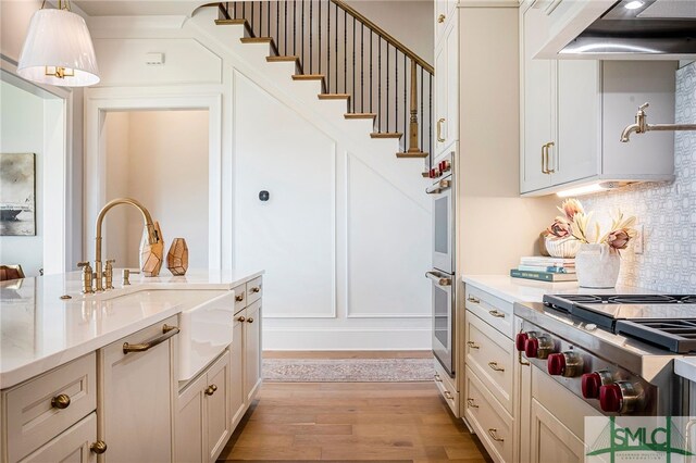 kitchen with exhaust hood, stainless steel gas cooktop, light hardwood / wood-style floors, hanging light fixtures, and sink