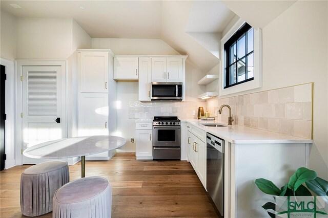 kitchen with white cabinets, hardwood / wood-style floors, appliances with stainless steel finishes, sink, and decorative backsplash