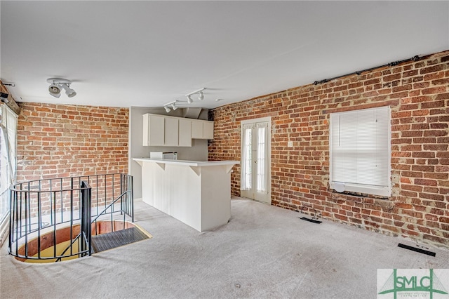 interior space featuring a kitchen bar, brick wall, kitchen peninsula, and light carpet