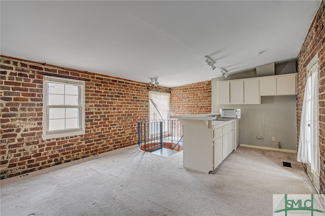 kitchen featuring white cabinetry, brick wall, kitchen peninsula, and light colored carpet