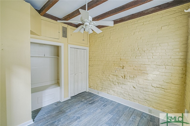 unfurnished bedroom with wood-type flooring, ceiling fan, beam ceiling, and brick wall