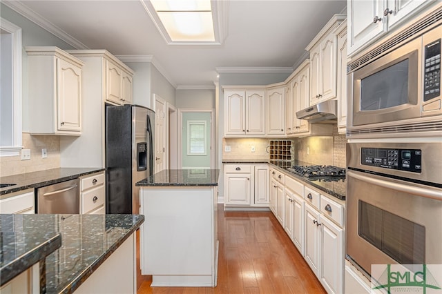 kitchen featuring dark stone countertops, ornamental molding, a kitchen island, light hardwood / wood-style floors, and stainless steel appliances