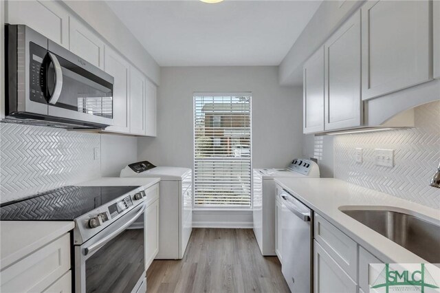 kitchen with light hardwood / wood-style floors, white cabinetry, stainless steel appliances, sink, and washing machine and clothes dryer