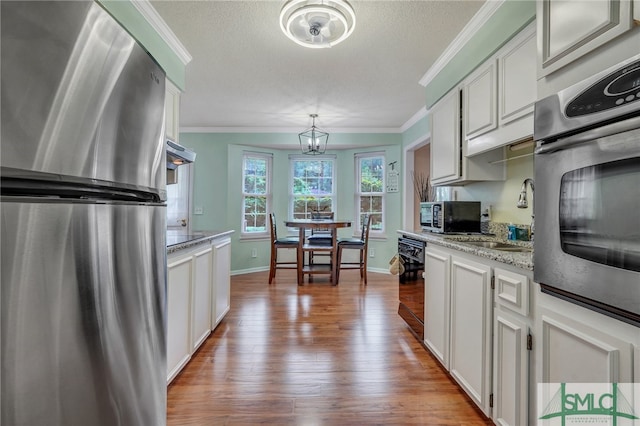 kitchen with light hardwood / wood-style flooring, stainless steel appliances, ornamental molding, and white cabinetry