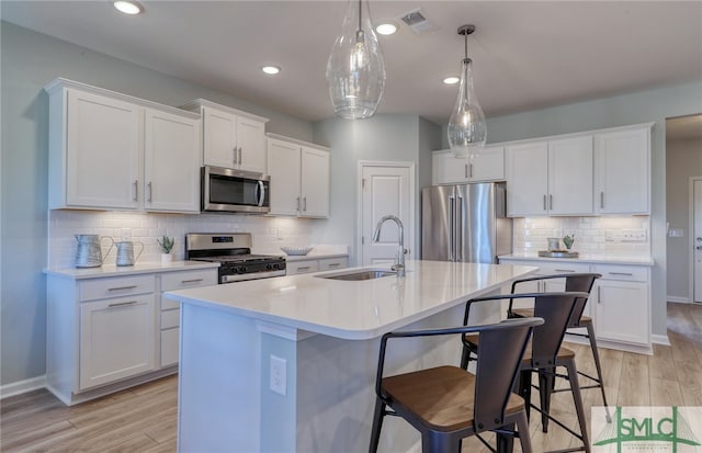 kitchen featuring white cabinetry, stainless steel appliances, light hardwood / wood-style flooring, decorative light fixtures, and sink