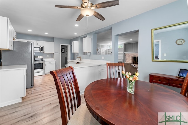 dining room with sink, ceiling fan, a brick fireplace, and light hardwood / wood-style flooring