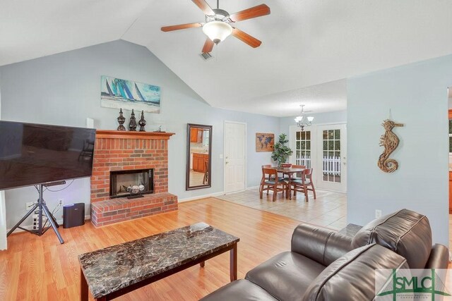 living room with ceiling fan with notable chandelier, light hardwood / wood-style floors, lofted ceiling, and a brick fireplace