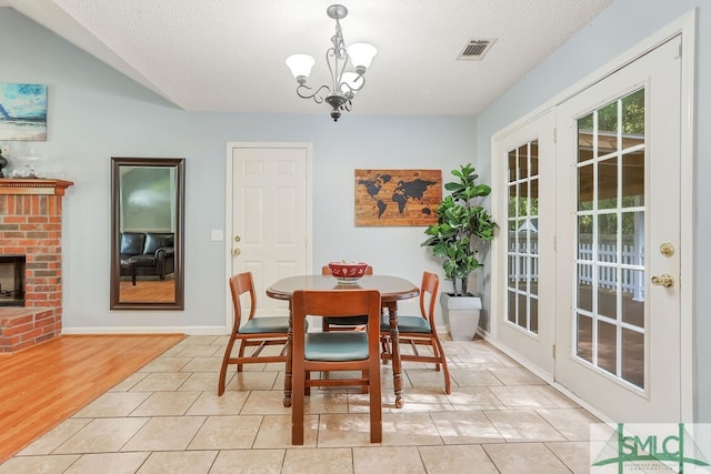 dining area with a textured ceiling, light wood-type flooring, an inviting chandelier, and a brick fireplace