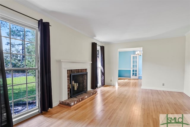 unfurnished living room featuring a brick fireplace, a notable chandelier, crown molding, and light hardwood / wood-style floors