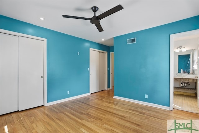 unfurnished bedroom featuring ensuite bathroom, ceiling fan, multiple closets, and light hardwood / wood-style flooring