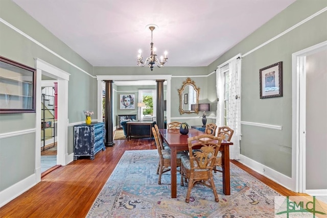 dining space featuring wood-type flooring, a notable chandelier, and ornate columns