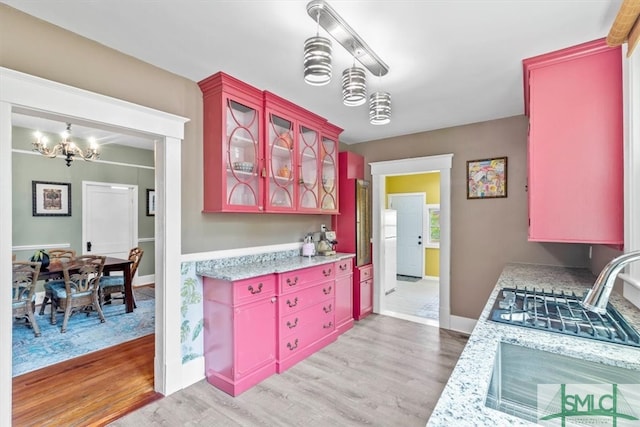 kitchen featuring light stone countertops, sink, decorative light fixtures, a chandelier, and light wood-type flooring