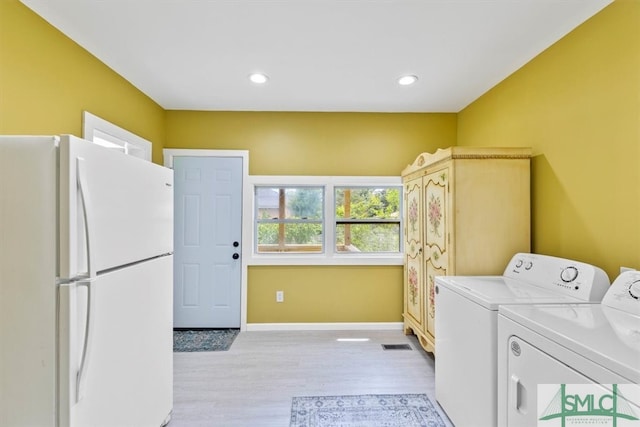 laundry room featuring light wood-type flooring, washer and clothes dryer, and cabinets