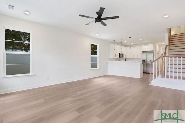 unfurnished living room with light wood-type flooring, a healthy amount of sunlight, and ceiling fan