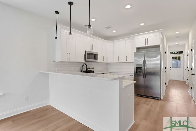 kitchen featuring light wood-type flooring, stainless steel appliances, white cabinets, kitchen peninsula, and decorative light fixtures