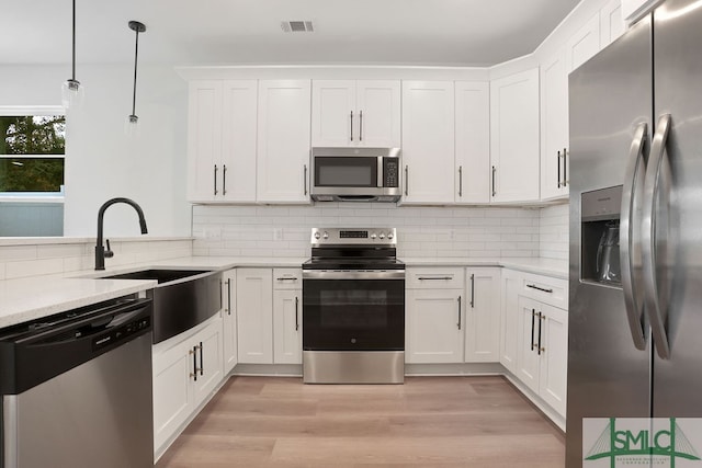 kitchen featuring light stone counters, stainless steel appliances, white cabinetry, light hardwood / wood-style flooring, and decorative light fixtures