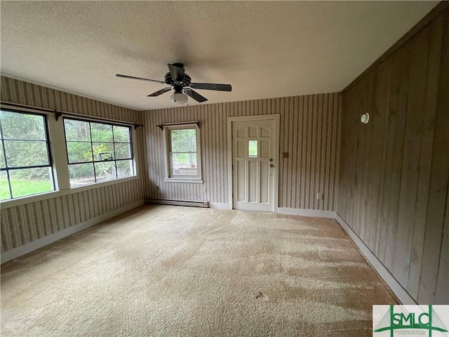 unfurnished room with ceiling fan, wood walls, carpet flooring, a textured ceiling, and a baseboard heating unit