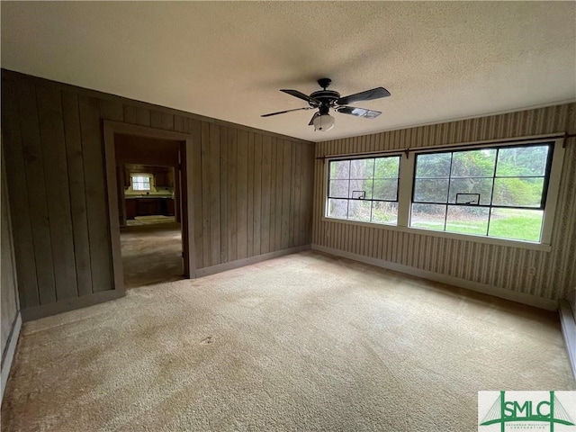 spare room featuring wooden walls, ceiling fan, light colored carpet, and a textured ceiling