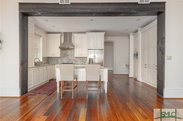 kitchen with a breakfast bar, wall chimney exhaust hood, a kitchen island, stainless steel appliances, and dark hardwood / wood-style floors