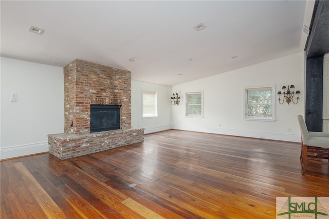 unfurnished living room featuring wood-type flooring, plenty of natural light, vaulted ceiling, and a brick fireplace