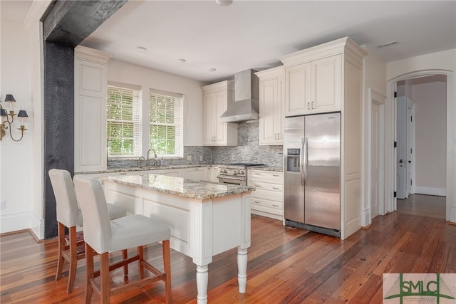 kitchen with dark wood-type flooring, appliances with stainless steel finishes, a center island, light stone countertops, and a kitchen bar