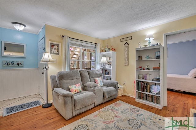 living room with ornamental molding, wooden walls, a textured ceiling, and hardwood / wood-style flooring