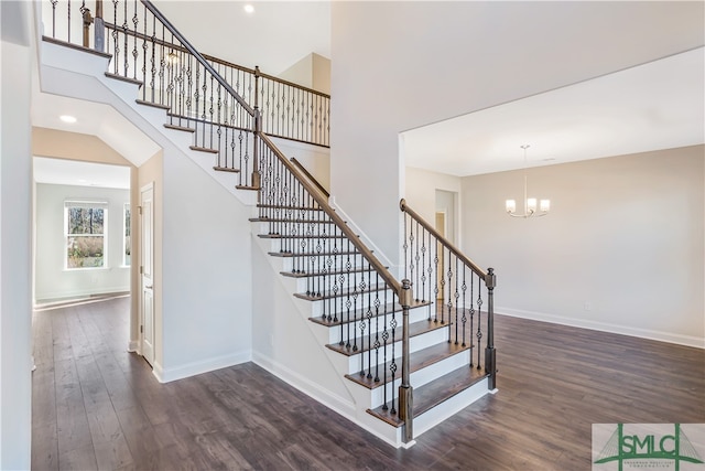 stairs with a high ceiling, hardwood / wood-style flooring, and a notable chandelier