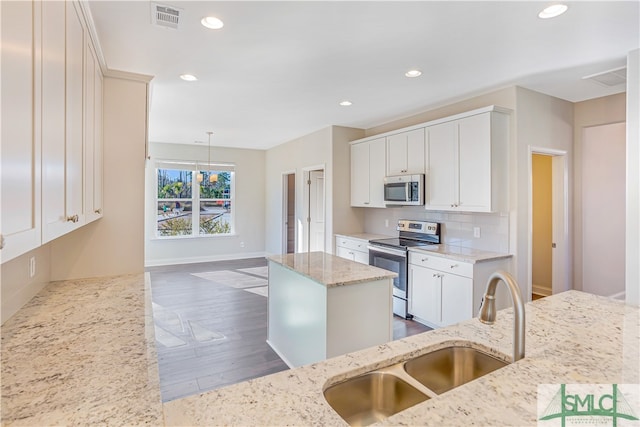 kitchen with light stone countertops, appliances with stainless steel finishes, sink, a kitchen island, and hanging light fixtures