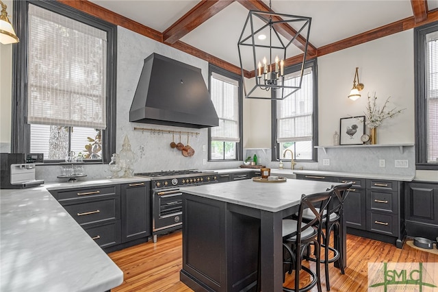 kitchen featuring a chandelier, high end stove, a center island, wall chimney range hood, and light hardwood / wood-style flooring