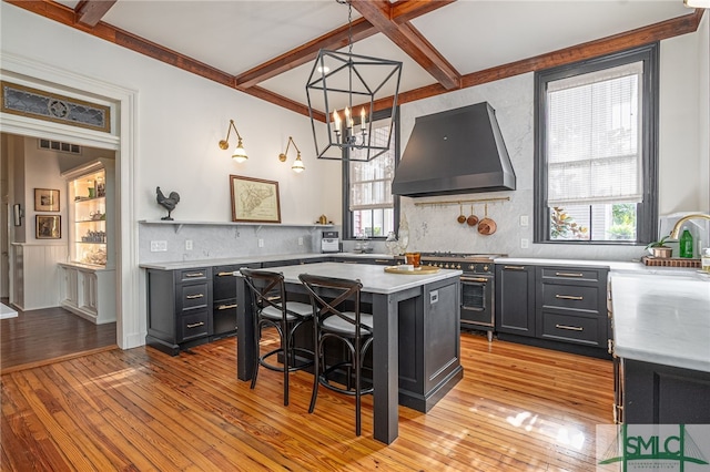 kitchen featuring a kitchen island, decorative light fixtures, wall chimney range hood, a breakfast bar, and light wood-type flooring