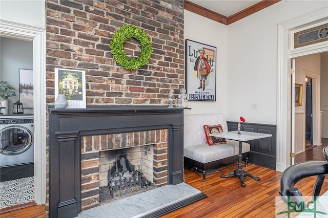 living room with wood-type flooring, crown molding, washer / dryer, and a brick fireplace