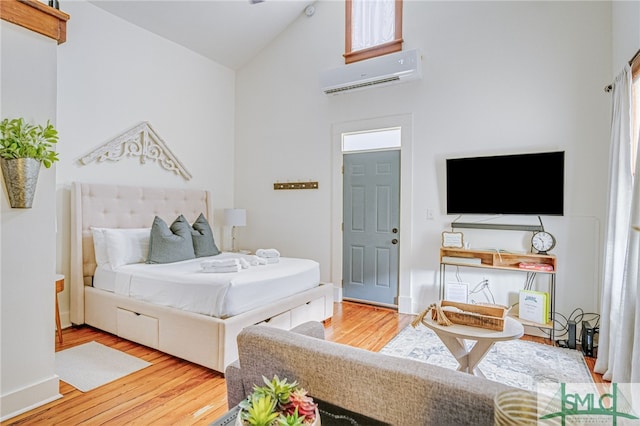 bedroom with hardwood / wood-style floors, high vaulted ceiling, and a wall mounted AC