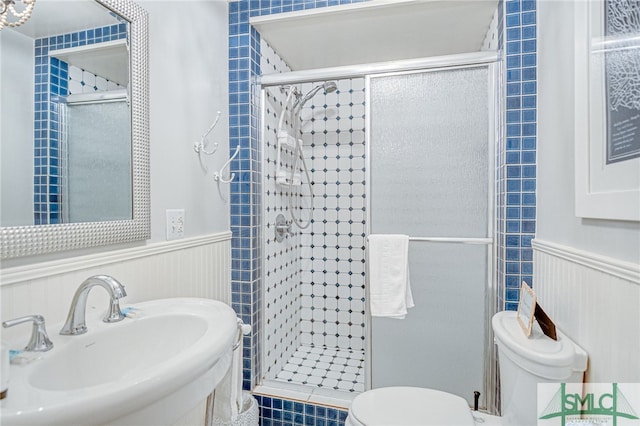 bathroom featuring a shower with door, toilet, and sink