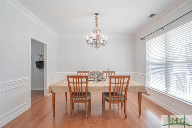 dining space featuring crown molding, an inviting chandelier, and light hardwood / wood-style flooring