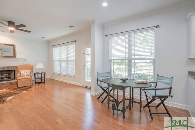 dining area featuring ceiling fan, a fireplace, light wood-type flooring, and ornamental molding