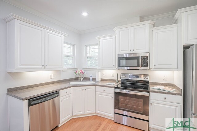 kitchen featuring sink, white cabinetry, stainless steel appliances, light wood-type flooring, and crown molding