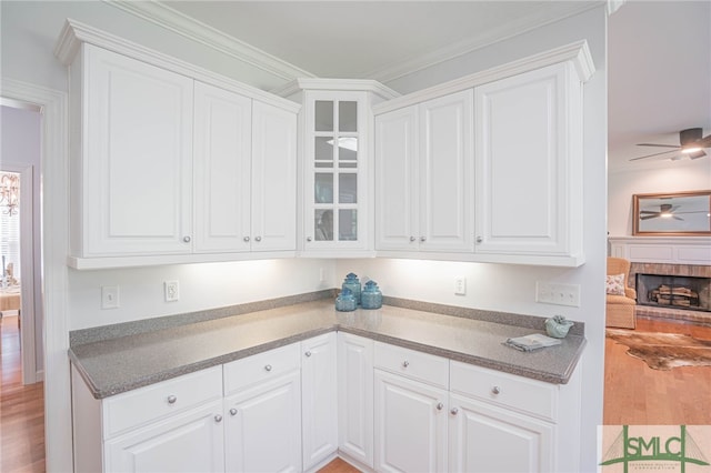 kitchen with ceiling fan, a brick fireplace, light hardwood / wood-style floors, and white cabinetry