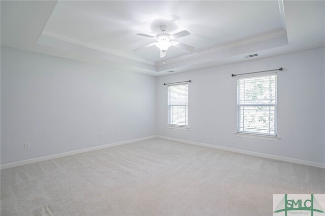 empty room featuring a raised ceiling, ornamental molding, ceiling fan, and light colored carpet