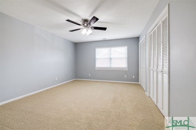 unfurnished bedroom featuring light carpet, two closets, ceiling fan, and a textured ceiling