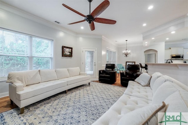 living area featuring arched walkways, ornamental molding, light wood-type flooring, and visible vents